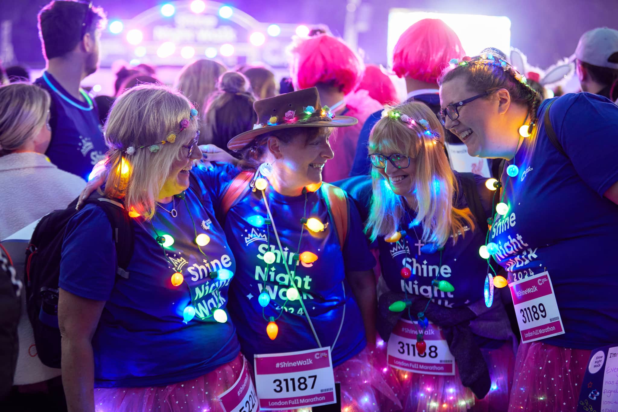 A group of 4 shine night walk participants lit up with fairy lights and smiling together.