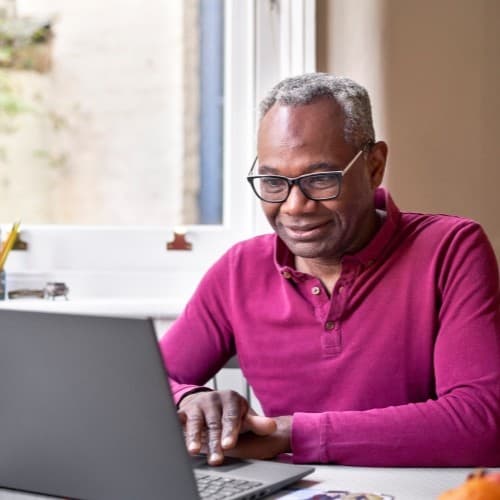 An image of a man in a red shirt sat looking down, partly smiling.