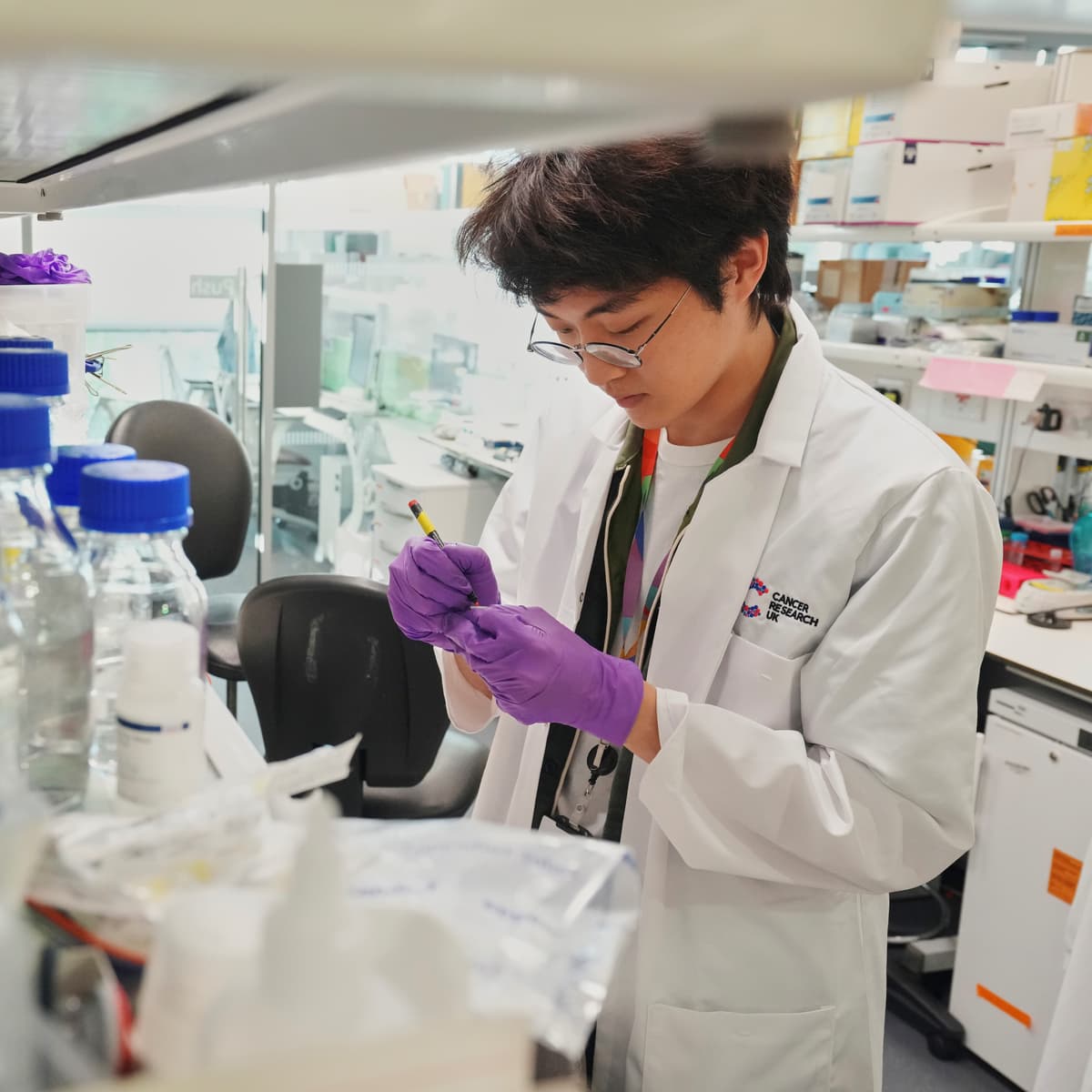 Researcher in a lab, in the forefront of the image are a number of bottles and containers.