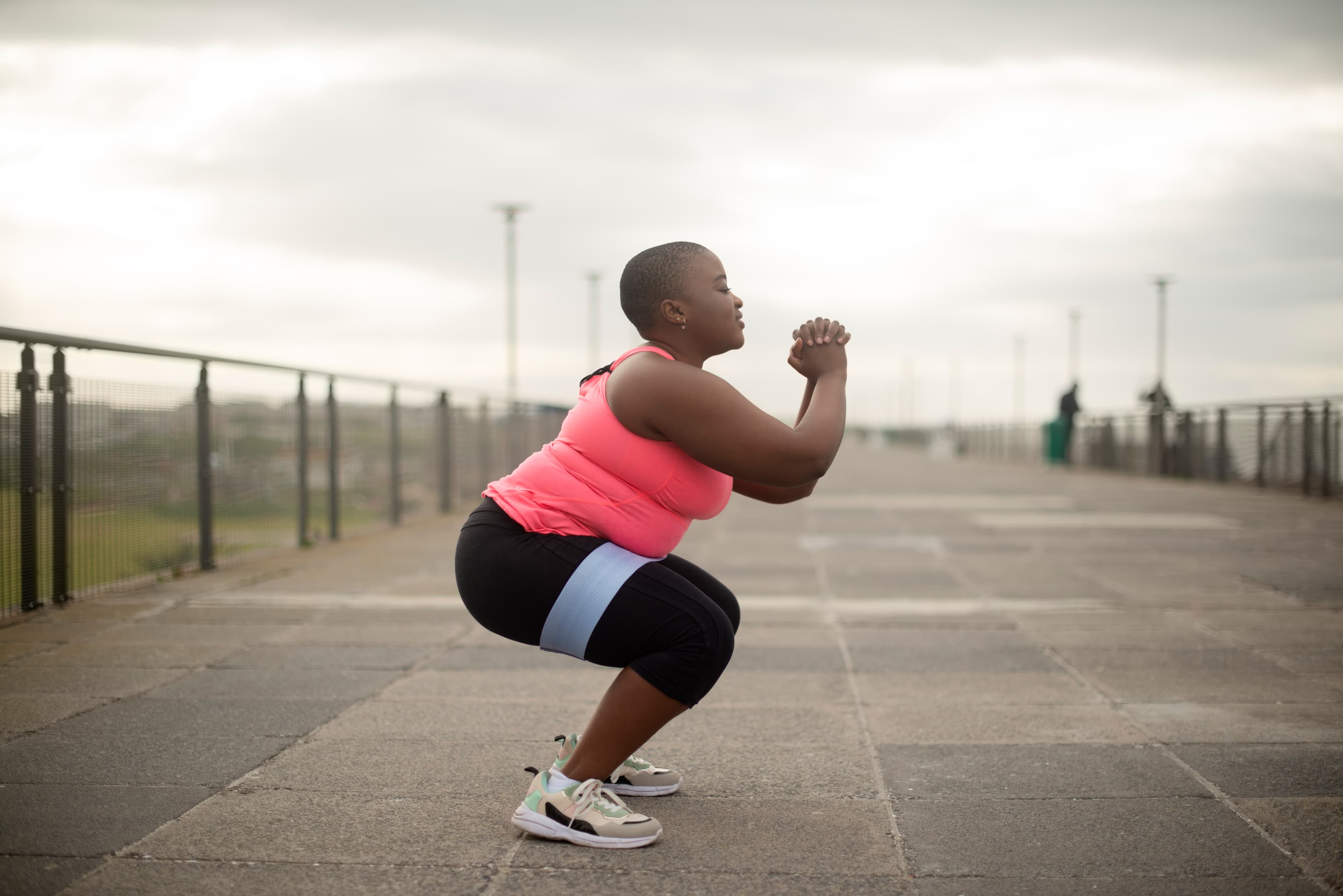 Side-shot of a woman doing a squat on concrete tiling outdoors.
