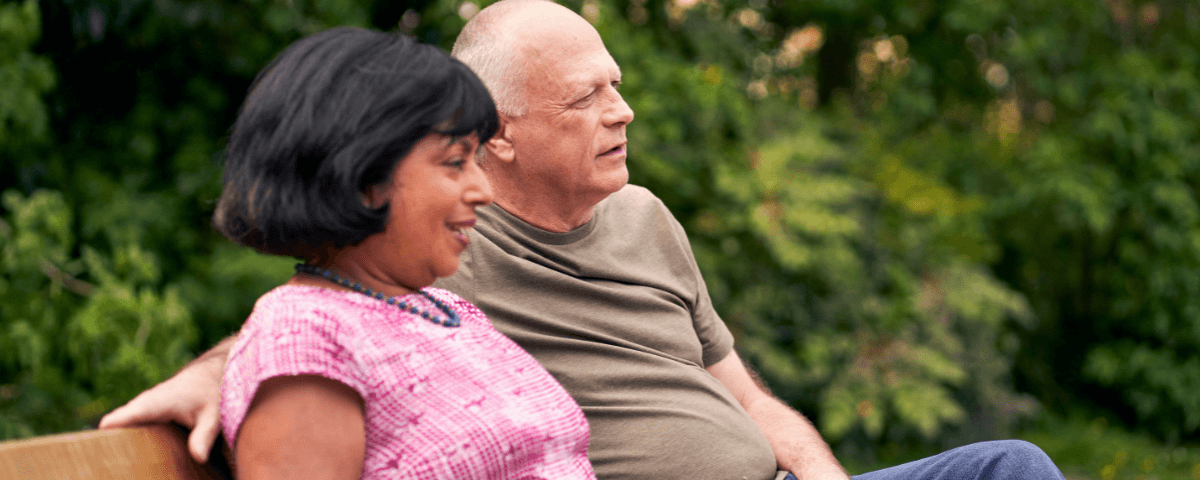 A man and a woman are sat on a bench outside talking to each other.