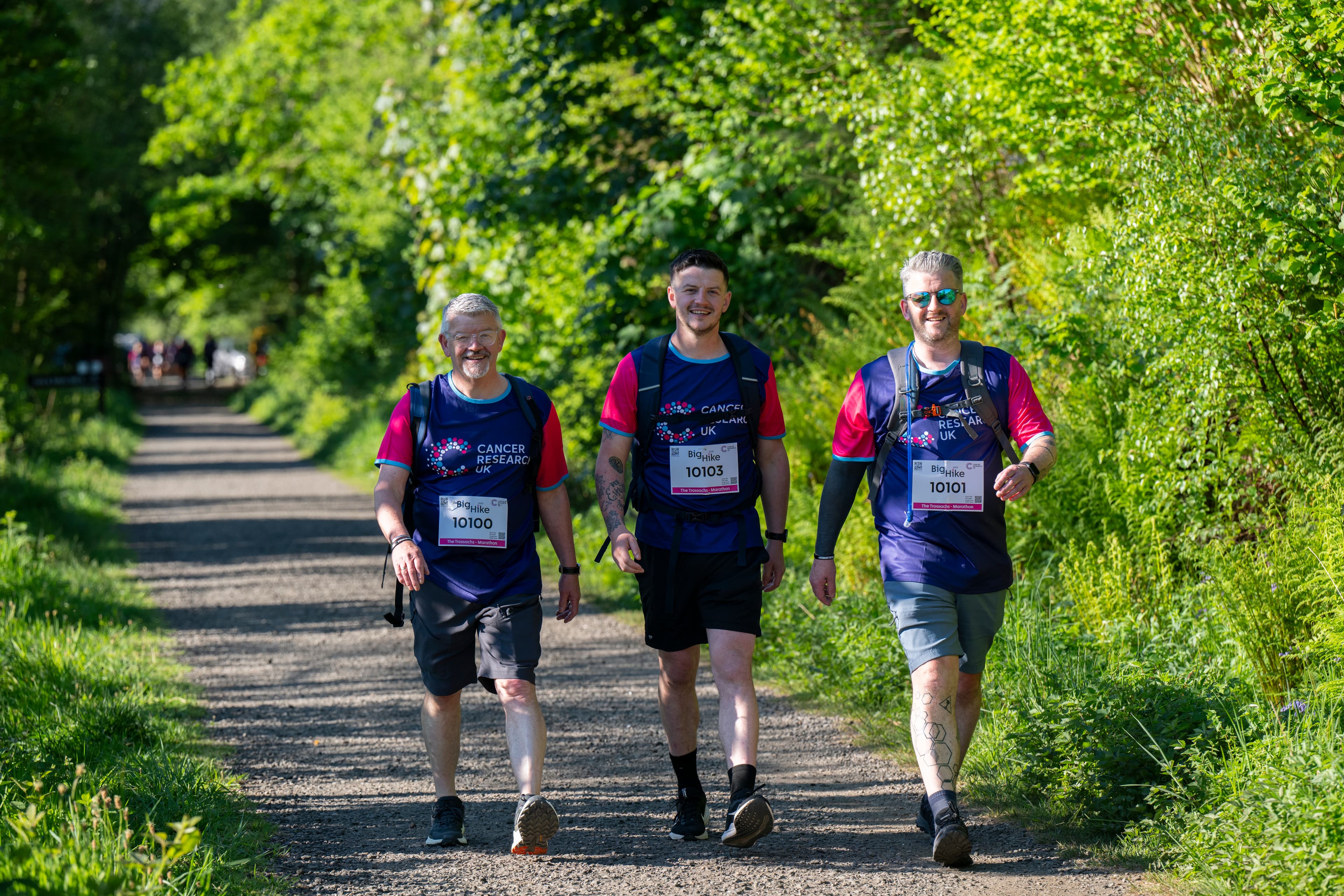 Three hikers walking along a leafy green trail.