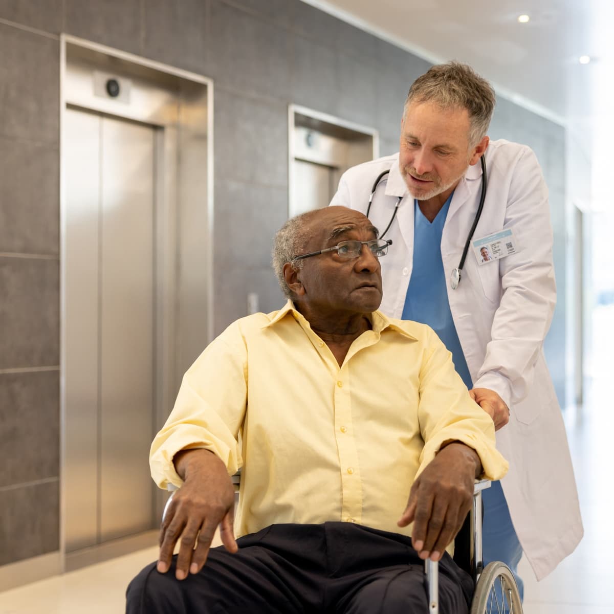 A clinician holding a wheelchair with a patient sitting in it, having a conversation.