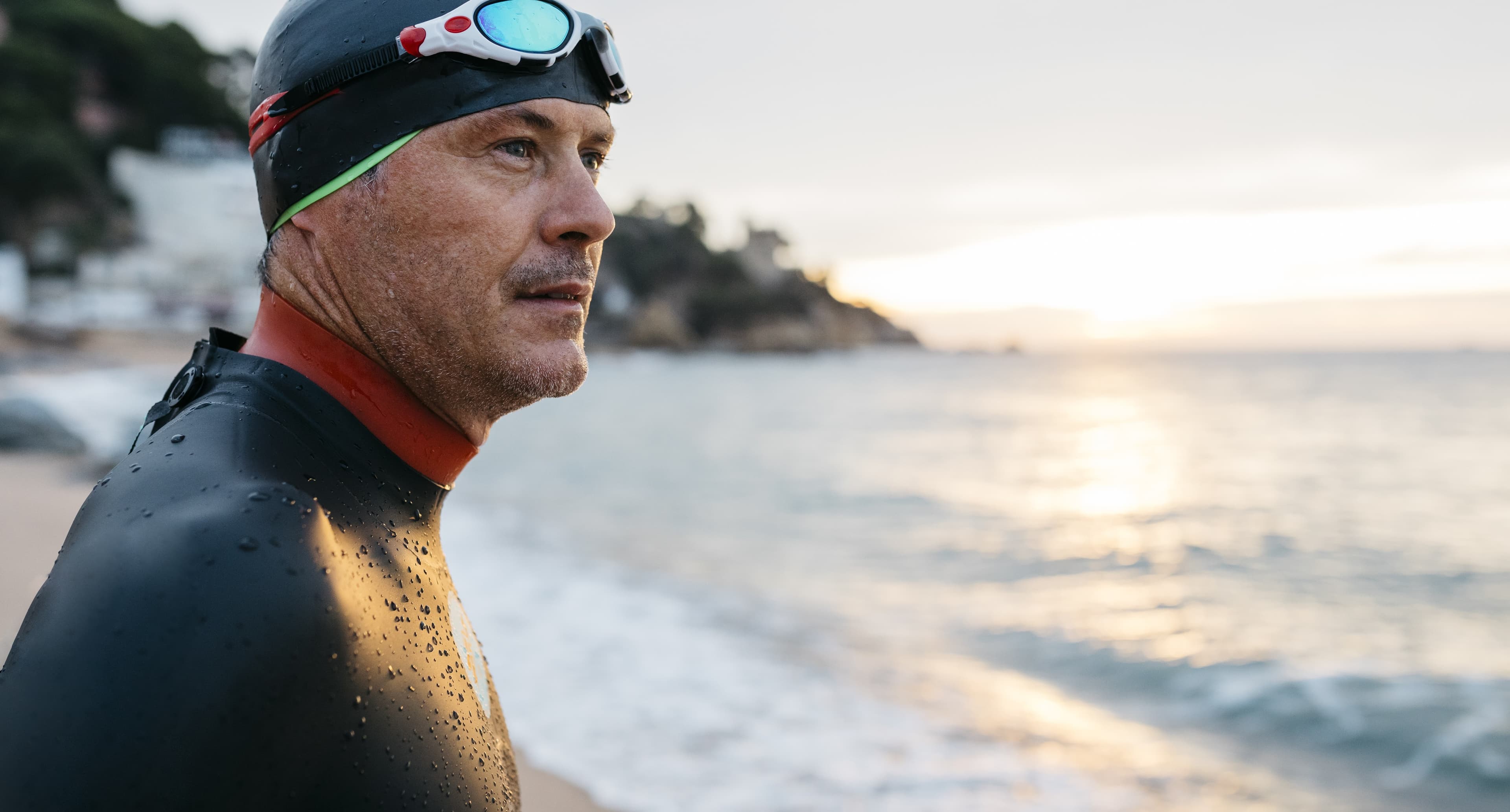 Close-up shot of a man wearing a swimming hat wetsuit and goggles by the sea.