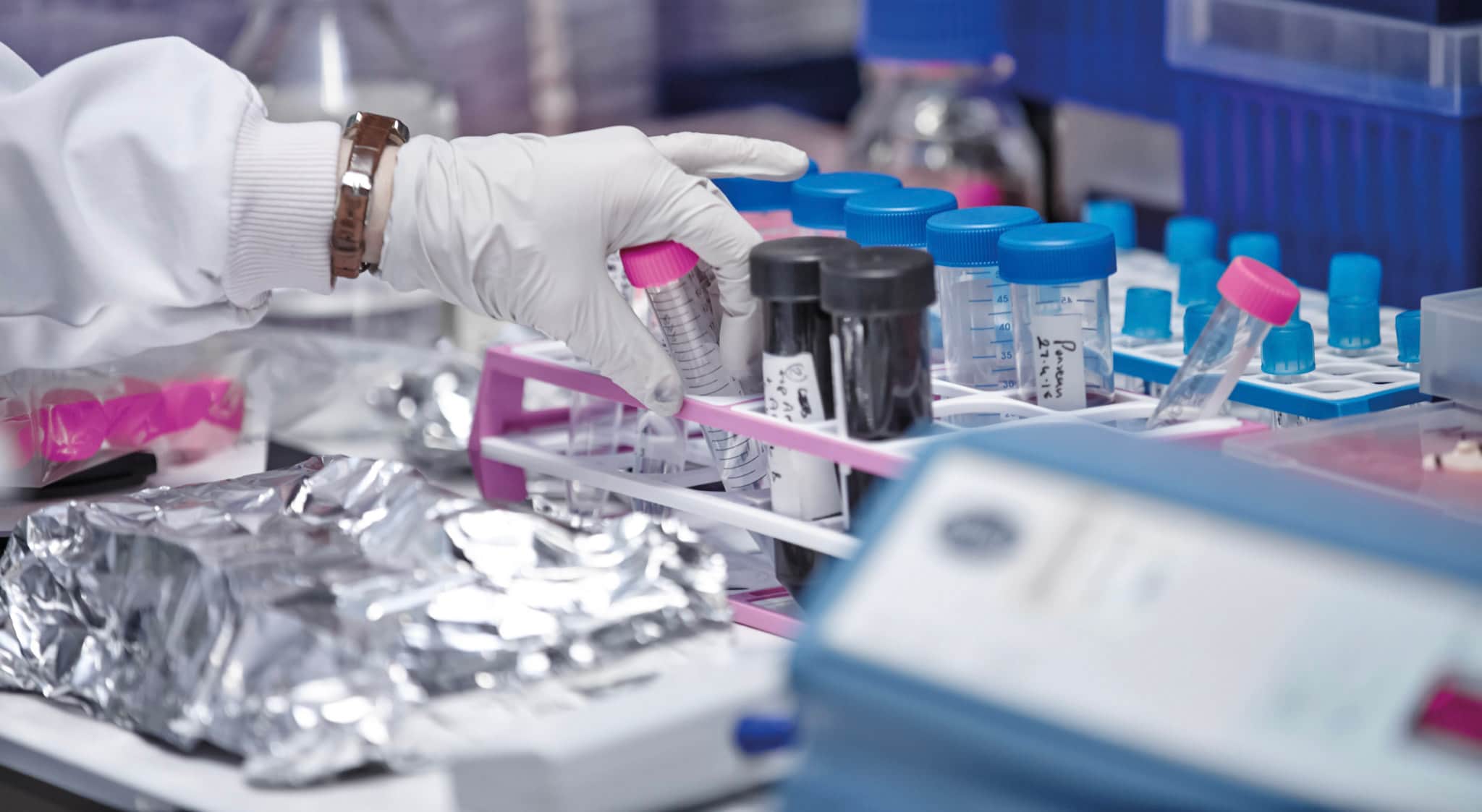 Image of lab equipment, with a hand reaching out to pick up a test tube.