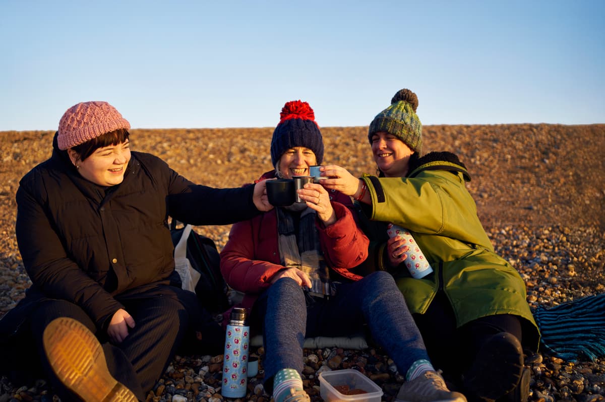 A photo of three people enjoying a hot drink outdoors.