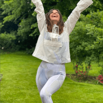 A picture of Dame Deborah James smiling with her hands up in the air.