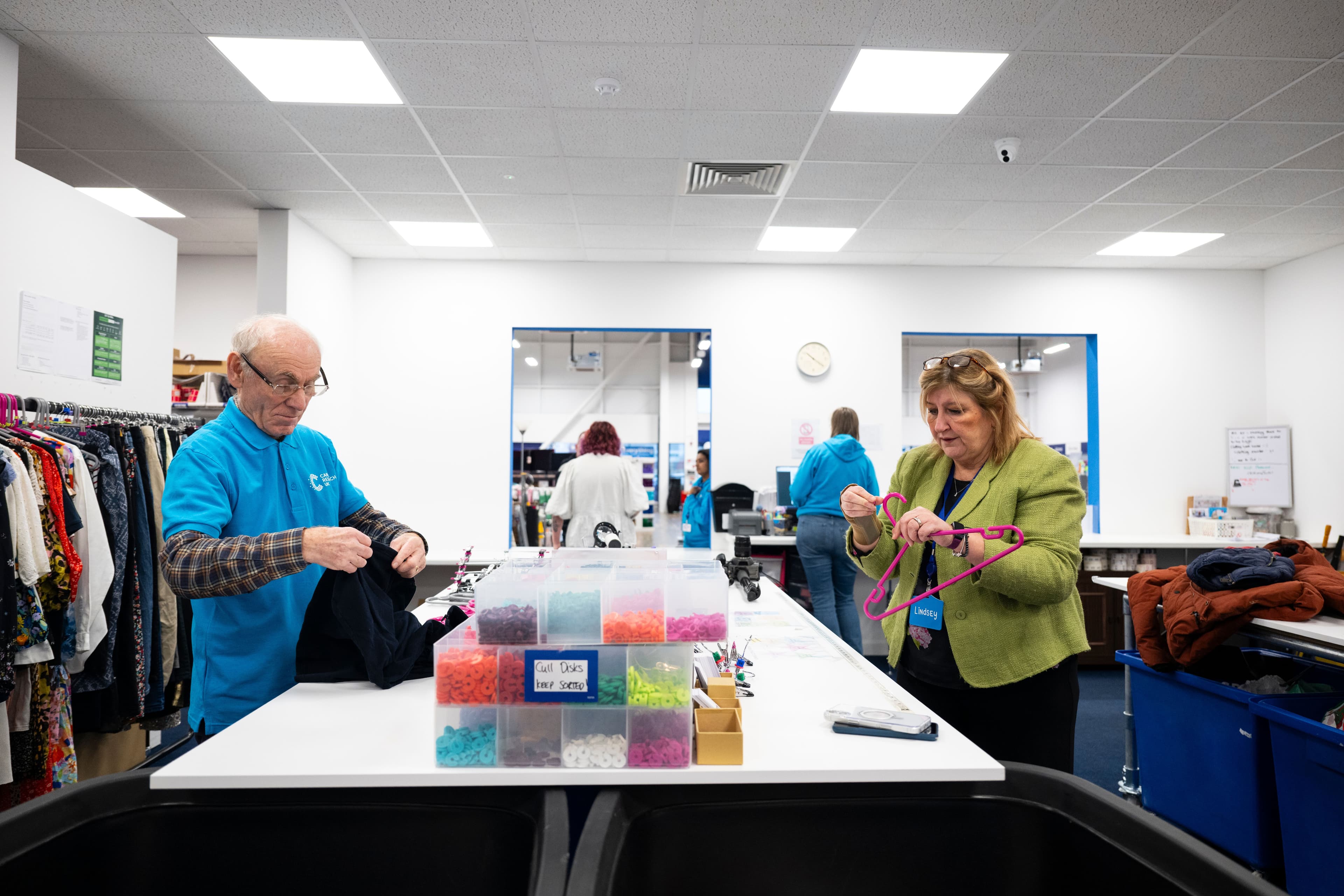 A man and woman hanging up clothing donations in a CRUK charity shop.