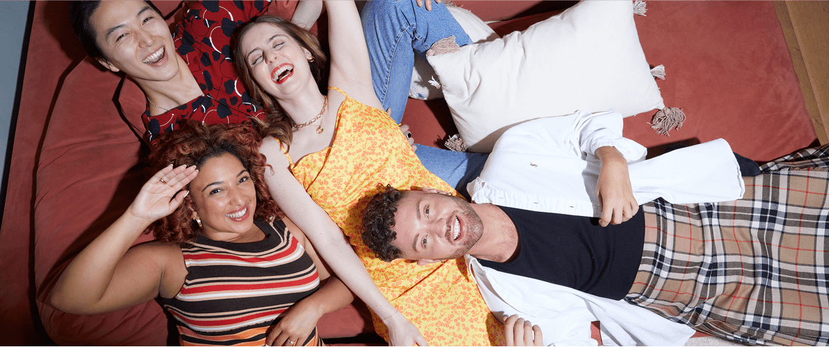 A photo of four people laying on a sofa smiling.