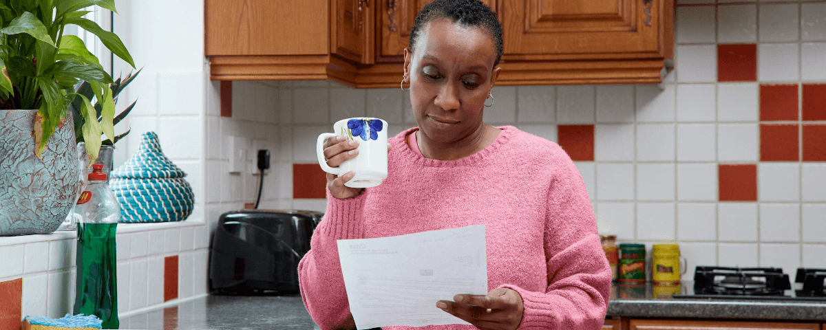 This photo shows a woman in the kitchen reading a breast or cervical screening invitation.