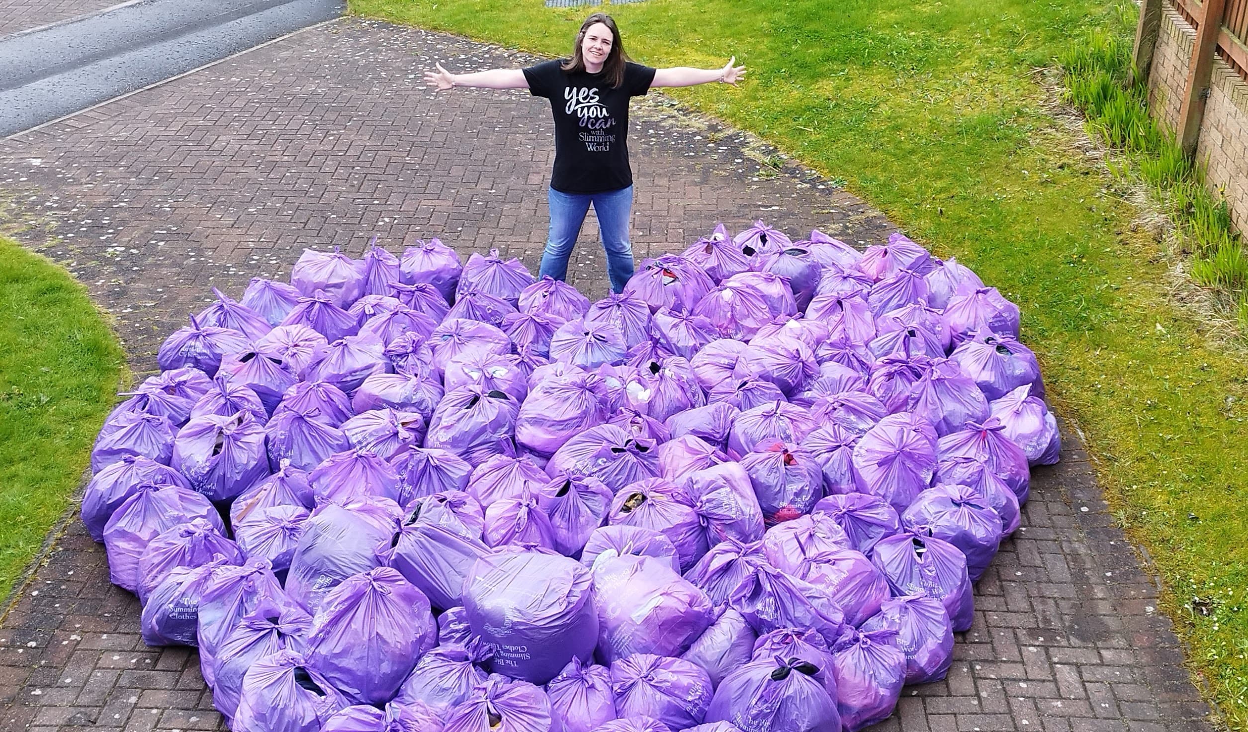 A woman posing with a heart shaped pile of donated clothing items as part of The Big Slimming World Clothes Throw.