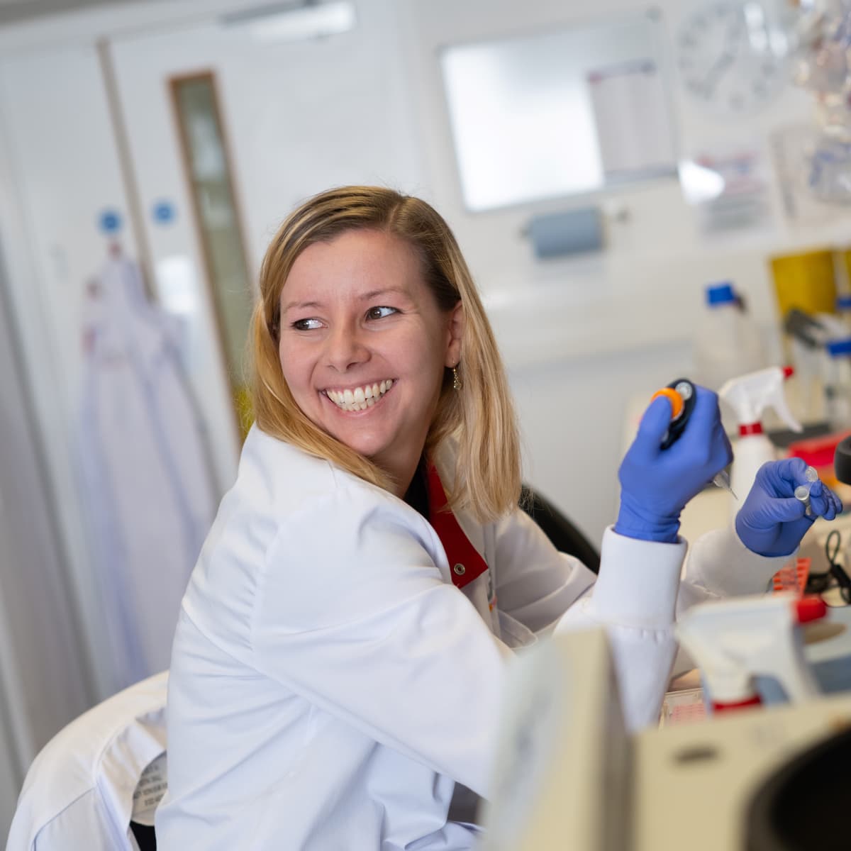 Research pipetting while sitting at a lab bench and smiling.