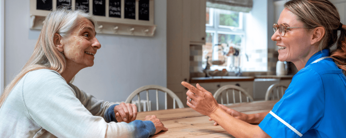 A woman talks to a medical professional about breast cancer in her home.