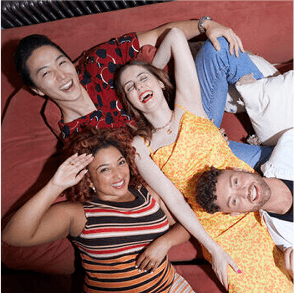 A photo of four people laying on a sofa smiling.