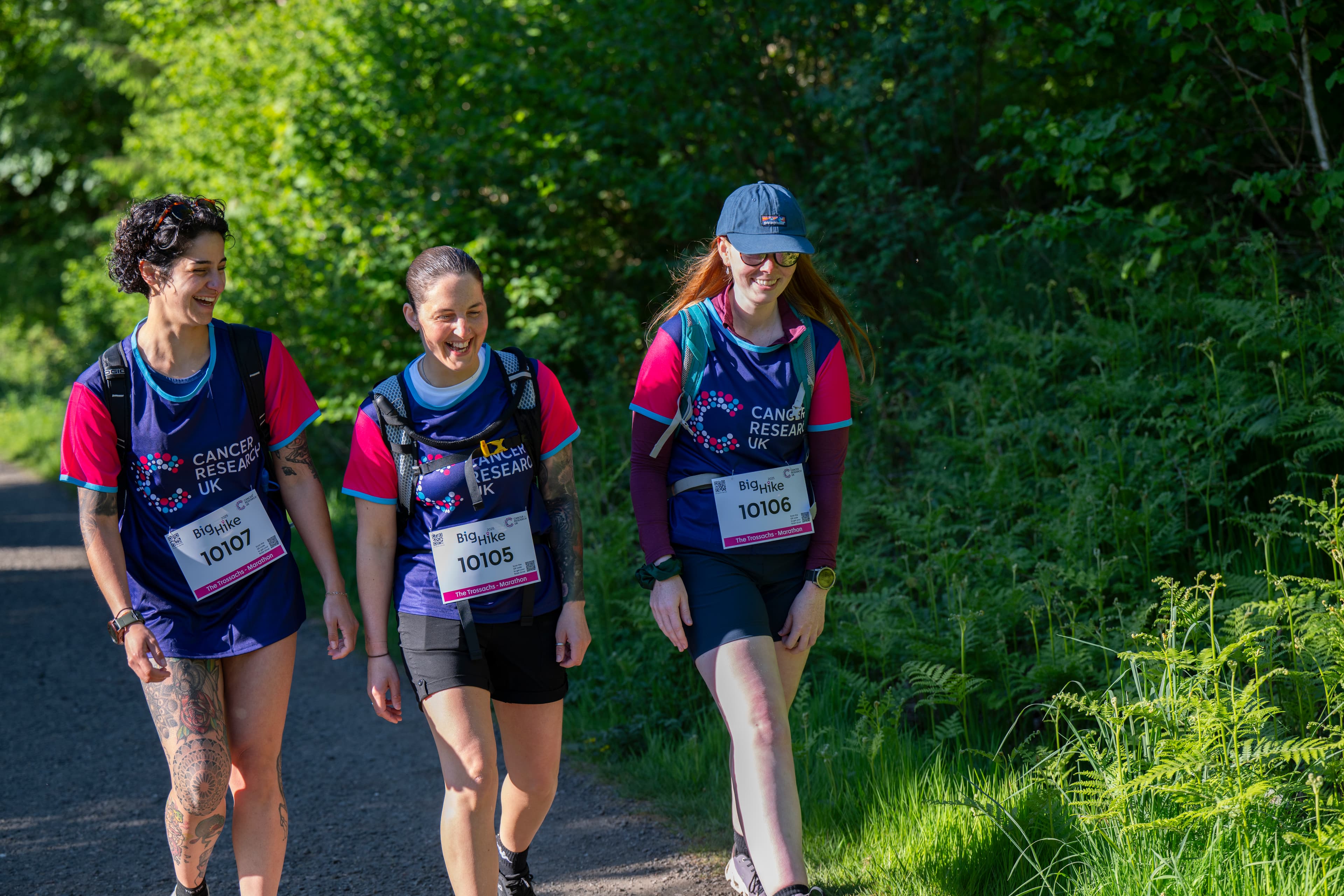 Three hikers smiling, walking along a leafy green trail.