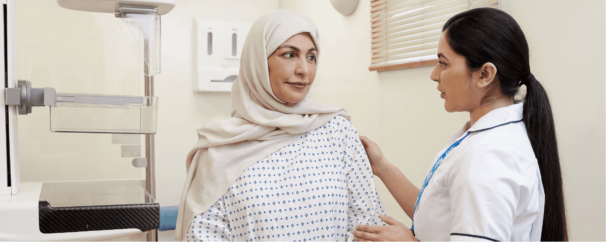 A photo of a mammographer / nurse with a patient, wearing a hospital gown, before a mammogram.